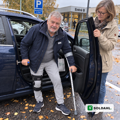 Mand med knæortose efter operation rejser sig ud af bilen med Stødro hægtet i låsebøjlen