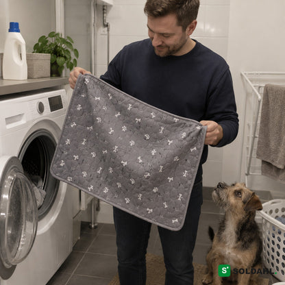 Mand tager den vaskede grå hvalpemåtte ud af vaskemaskinen, mens hunden kigger på
